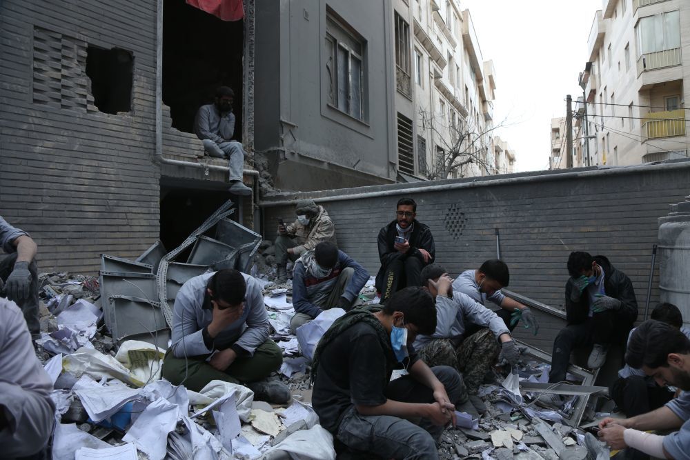 3月15日，在伊朗首都德黑兰的一处遇袭居民区，人们坐在一处建筑废墟上。