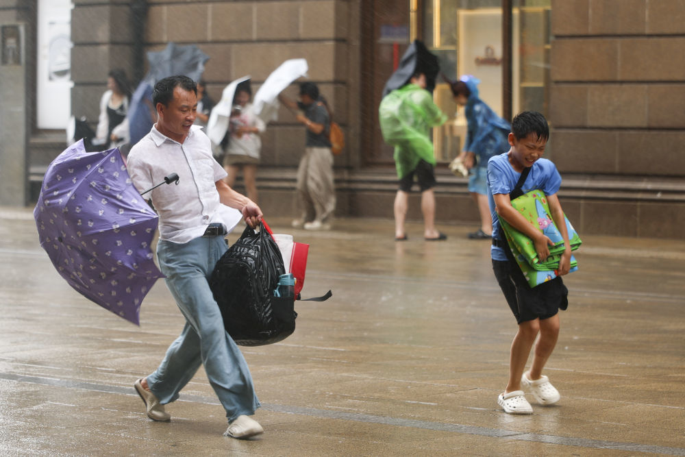 8月9日，在上海黄浦区南京东路上，父亲陪同孩子冒雨前行。新华社记者 王翔 摄
