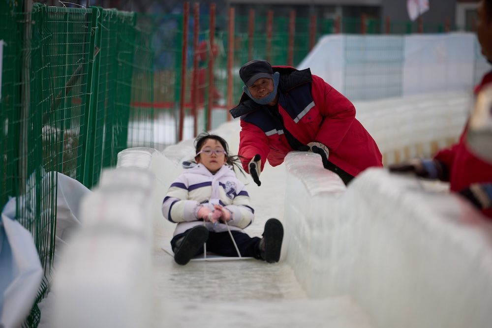 2026年1月16日，奥森公园雪场，一个工友在冰滑梯上为游客助力。
