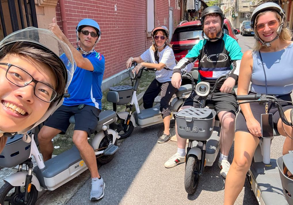 2025年8月底,外国游客在上海的弄堂里骑行电动车。新华社发