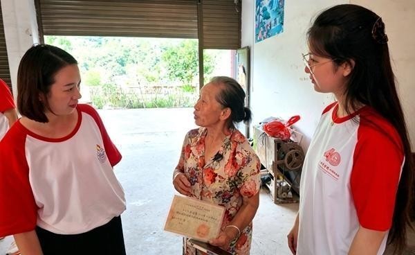 广西壮族自治区灌阳县排埠江村枫树脚屯村民李清鸾(右二)向北京城市学院师生展示捐赠红旗的证明材料。张泽阳供图