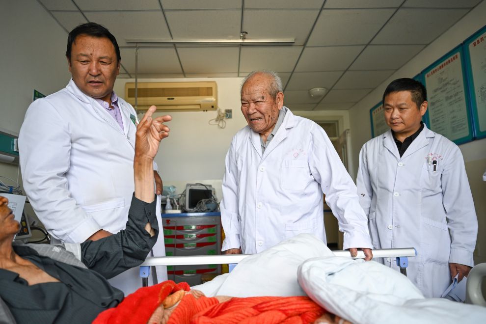 2026年7月30日，吴登云（中）在乌恰县人民医院住院楼和医院医生一起查房，碰到一位年近90岁的熟人患者。