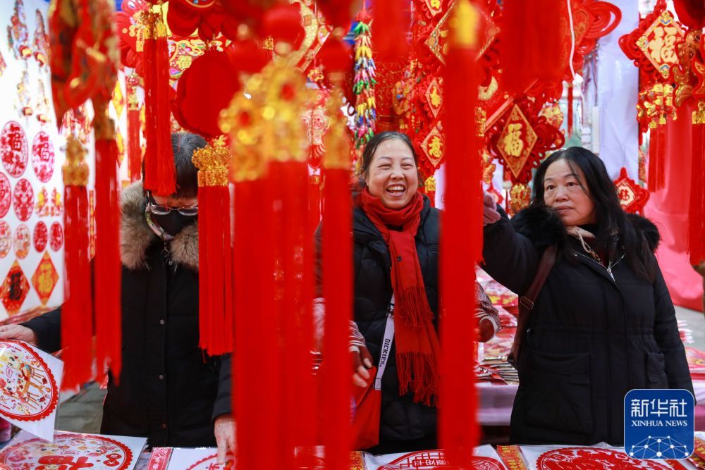 ↑ 1月22日，市民在贵州省都匀市文峰广场年画市场挑选春节饰品。新华社发（肖伟摄）