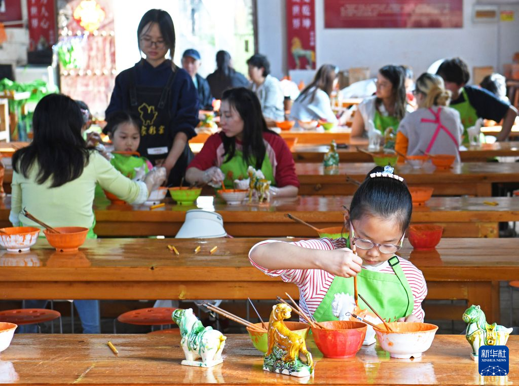 10月3日,小游客在河南省洛阳市孟津区朝阳镇南石山村“三彩小镇”体验唐三彩绘制技艺。新华社发(白水平摄)