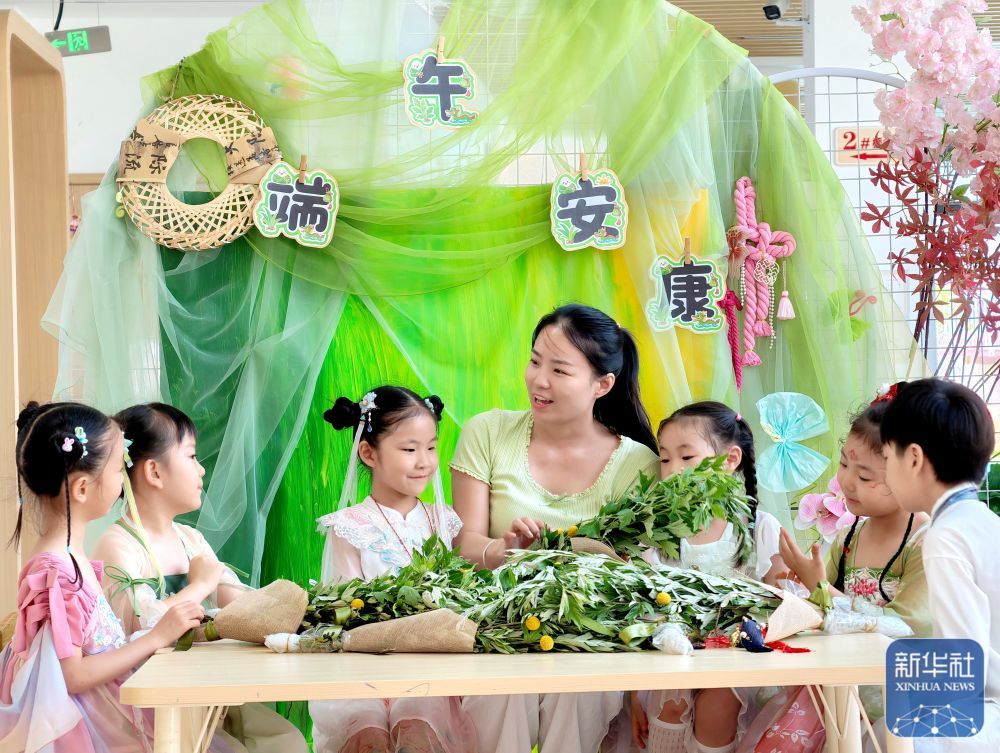 ↑ 6月17日,在河南省济源市第一幼儿园,老师教小朋友们制作艾草花束。新华社发(段二平摄)