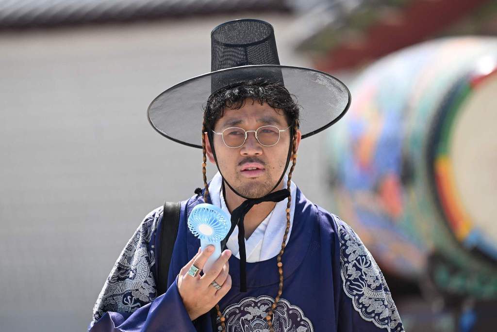 8月3日，韩国首尔，一名身着传统韩服的游客在景福宫使用便携风扇降温。视觉中国 图