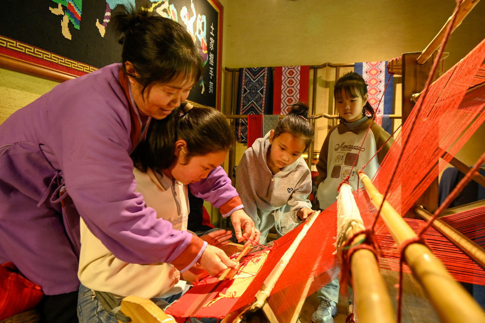 ↑4月3日，重庆市酉阳土家族苗族自治县桃花源景区非遗织锦工坊，小朋友们在非遗传承人的指导下学习土家织锦纺织技艺。新华社发（邱洪斌摄）