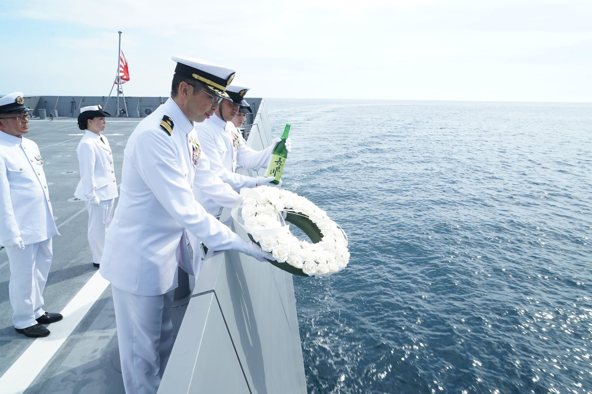海上自卫队“长良”号舰员向海中抛花环并倒清酒