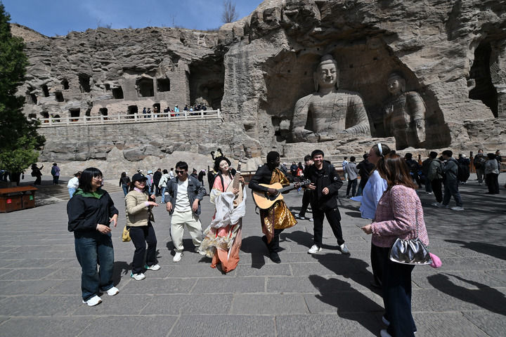 在云冈石窟，身着传统服装的演员和游客互动。（新华社记者詹彦 摄）