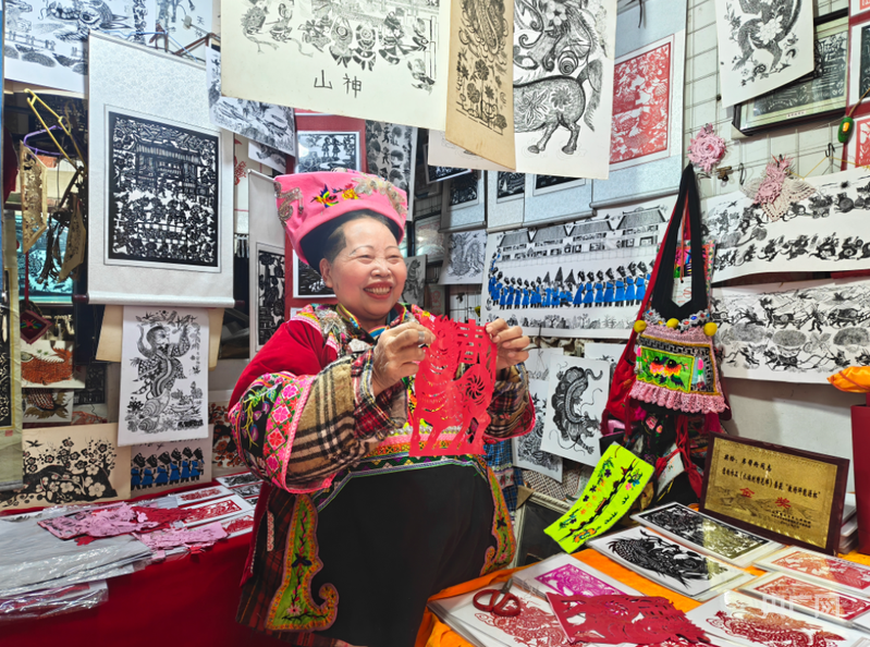 72岁的韦邦粉在剪纸店内向游客展示自己的马年剪纸作品（央广网记者 栾小琳 摄）
