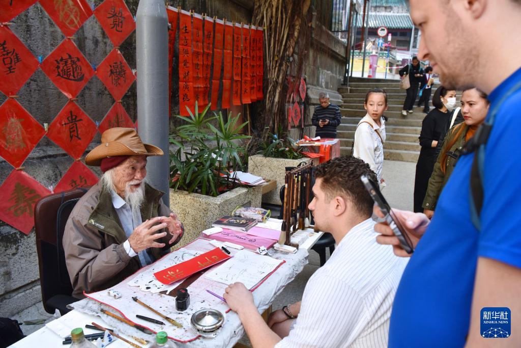 2月13日,在香港楼梯街,郭腾龙(左)为外国朋友讲解中文名字。新华社记者 陈铎 摄