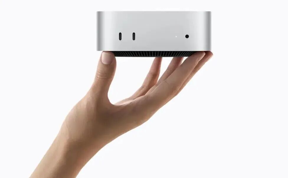 A person’s hand holds the silver Mac mini, showing its front ports.