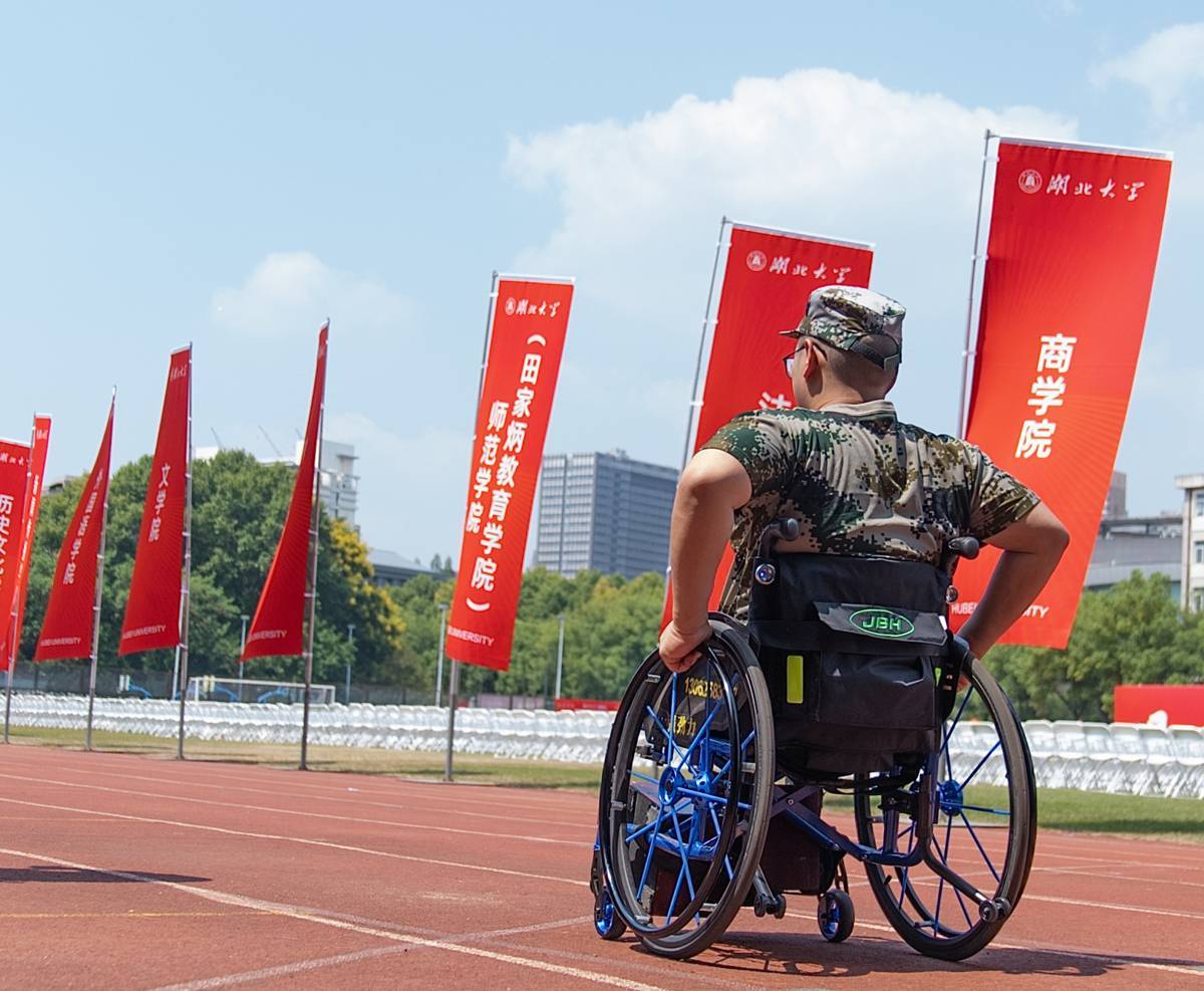 湖北大学运动场上,方宇翔转动轮椅,行进在红色跑道上,身旁林立着各学院红色道旗,他以轮椅为伴,投入大学军训。