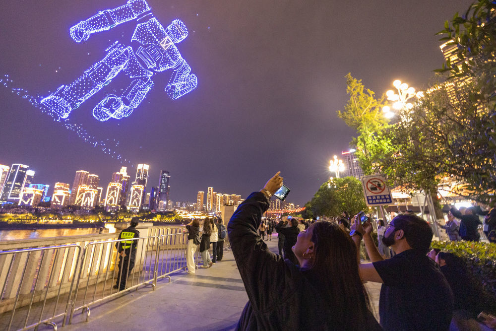 ↑ 4月22日，外籍游客在重庆市南岸区南滨路拍摄无人机灯光秀表演。