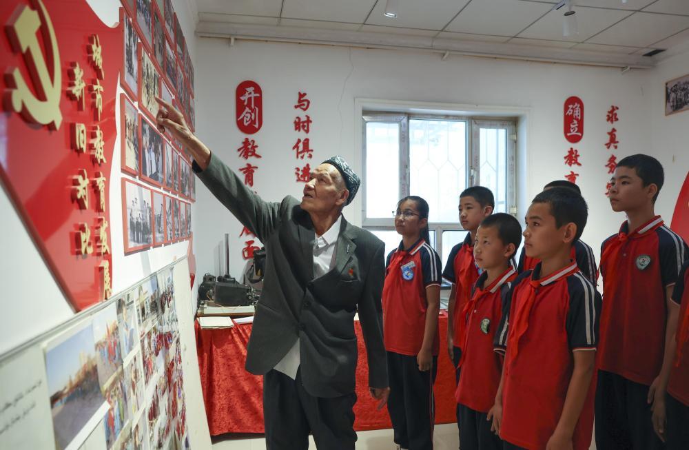 2026年6月24日，在位于新疆库尔勒市恰尔巴格乡萨依巴格村的“梨城记忆”文化小院，克热木&middot;木沙（左）在为前来参观的学生们讲述老照片背后的故事。新华社记者 王菲 摄