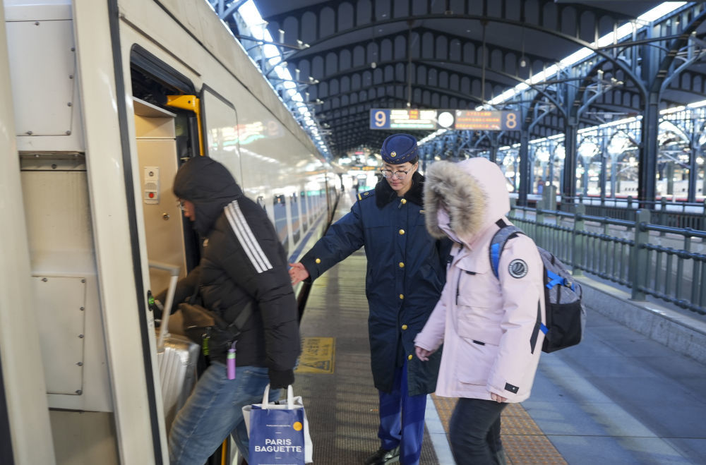 中国铁路哈尔滨局集团有限公司工作人员(中)在哈尔滨火车站为旅客服务。李昕洋 摄