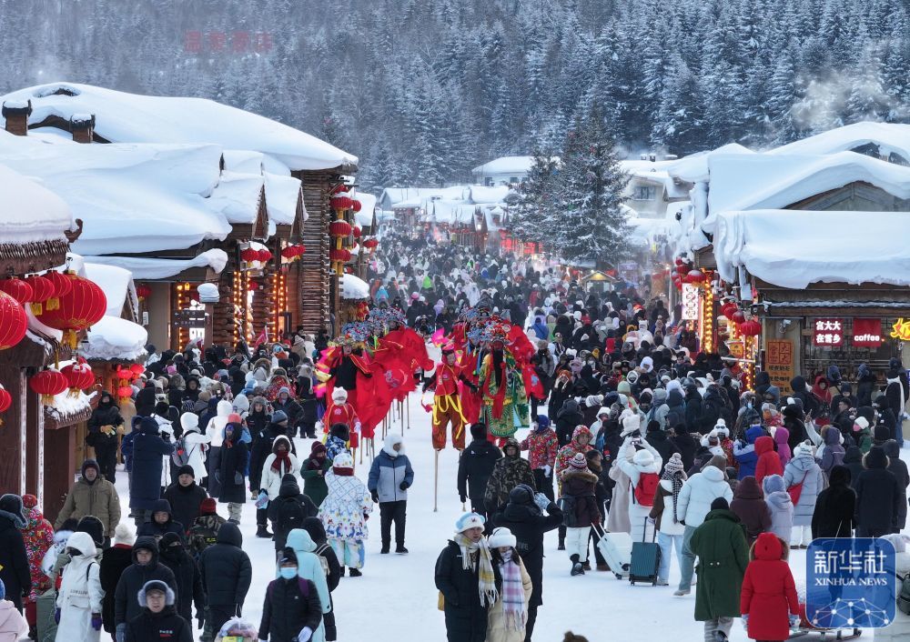 ↑ 1月1日,游客在位于黑龙江省牡丹江市的“中国雪乡”景区雪韵大街上欣赏踩高跷表演(无人机照片)。新华社发(孙庭义 摄)