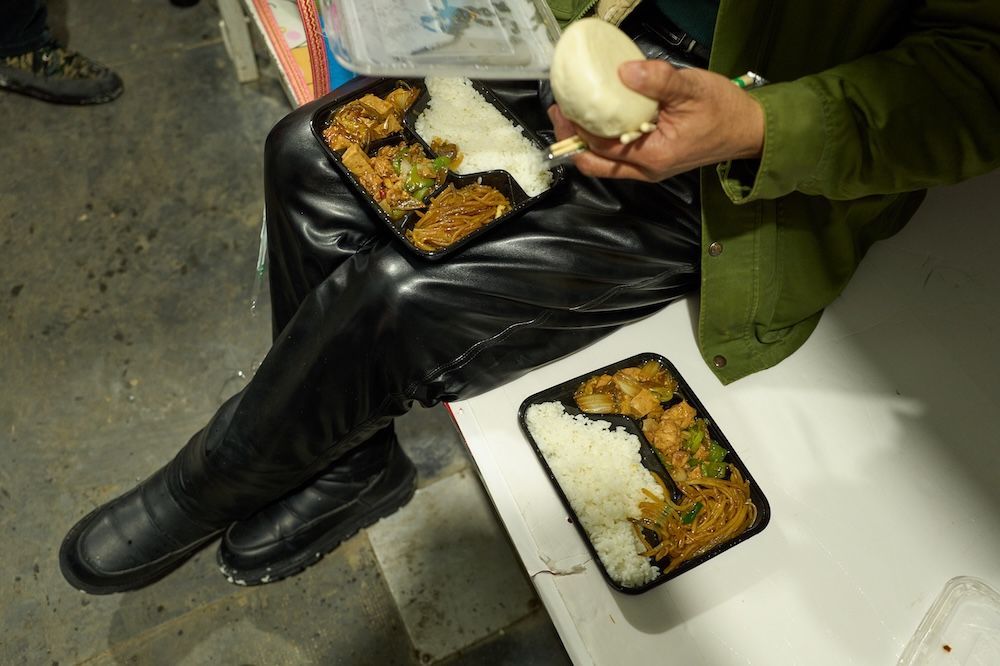 一位工友将盒饭放在腿上准备吃饭。
