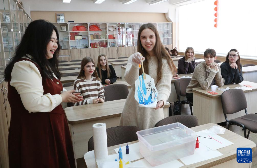 2月2日，在白俄罗斯首都明斯克，白俄罗斯国立外国语大学汉语言与文化系学生波林娜&middot;格里博克（前右）体验制作中国漆扇。 新华社发（任科夫摄）