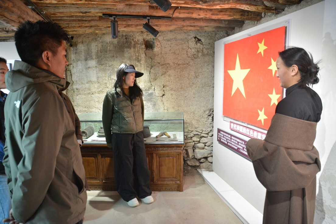 图为阿西的孙女次旺卓吉(右一)在雅安朵十八军营地旧址国旗展柜旁讲述这面国旗的故事。