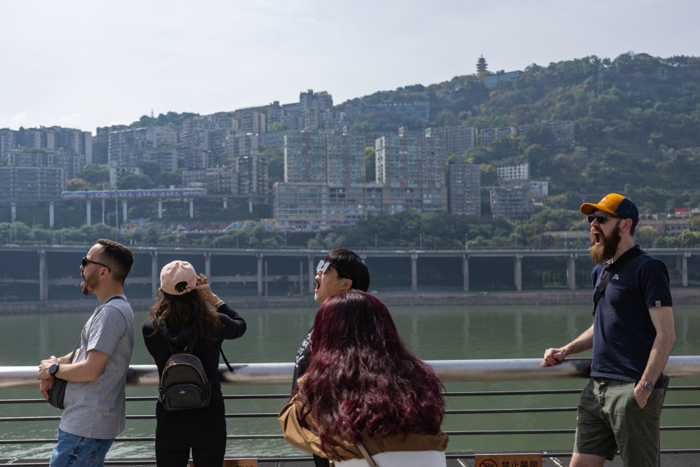 ↑ 4月23日，在重庆市两江新区，外籍游客摆出“吃”轻轨的姿势拍照。