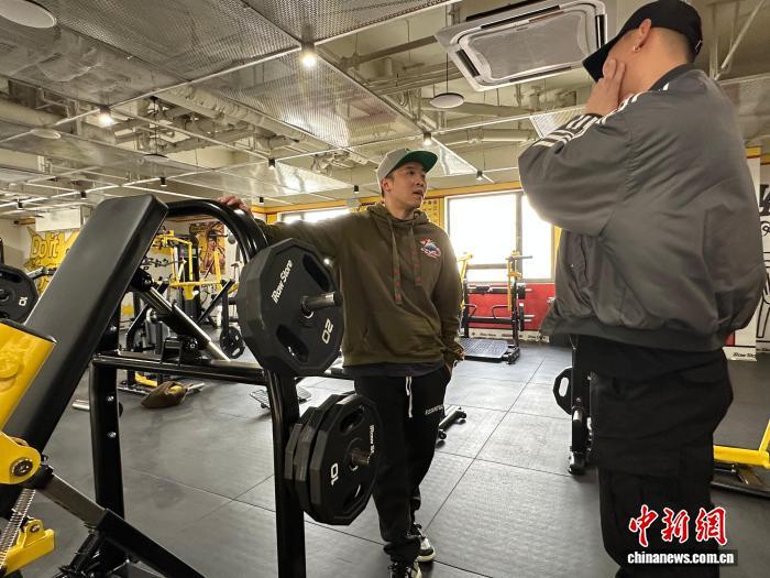 2月5日,王惟勋(左)在健身房与合作伙伴进行交流。 中新社记者 张一辰 摄