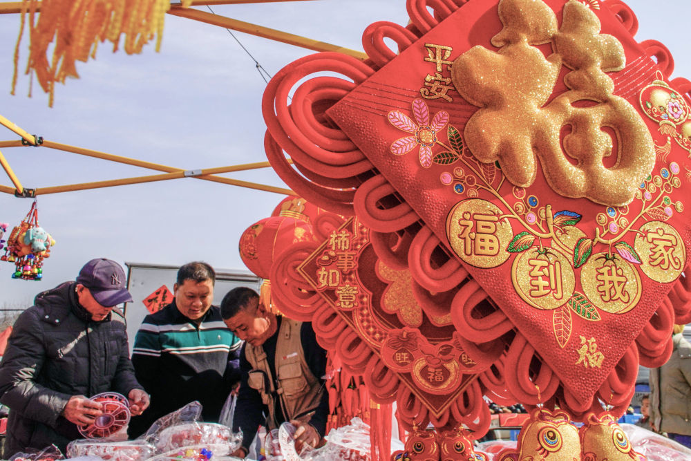 ↑ 2月14日，人们在北京市平谷区的年货大集选购饰品。新华社发（刘满仓摄）