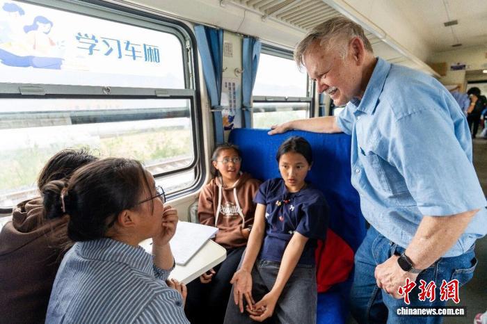 在四川凉山,潘维廉(右一)在穿行大凉山的公益慢火车上,与乘客深入交流,探寻这趟慢火车如何串联起乡村振兴的图景。徐讯 摄