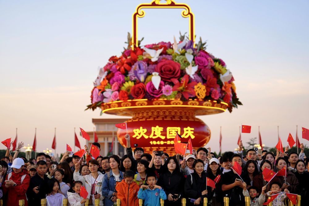 2025年10月1日，在北京天安门广场，人们观看升国旗仪式后挥舞国旗。