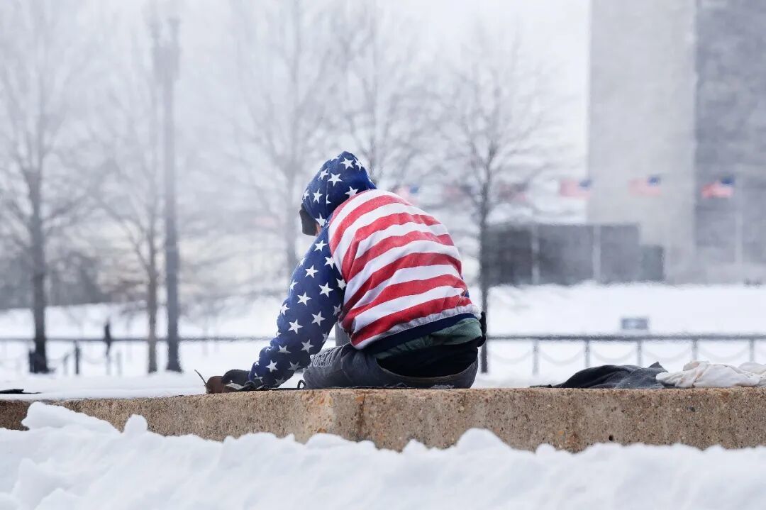 ·当地时间2026年1月26日,美国华盛顿特区,一场冬季暴风雪过后,一名无家可归者坐在暖气通风口上取暖。(视觉中国)