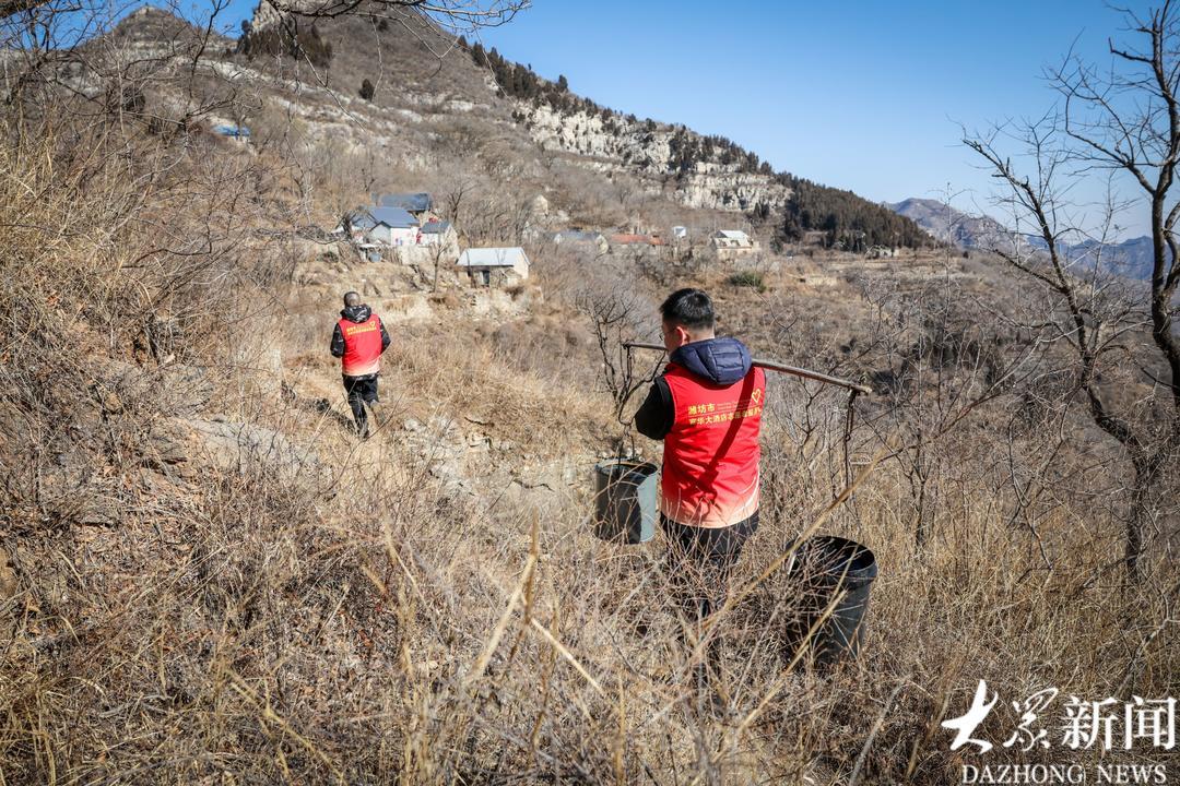 挑水的路不好走，两名志愿者换班挑。