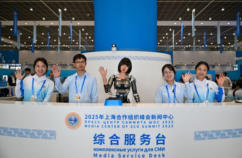 2025年8月28日，在2025年上海合作组织峰会新闻中心，可进行多种语言互动的人形机器人“小合”（中）与志愿者、工作人员一起在综合服务台欢迎到访记者。