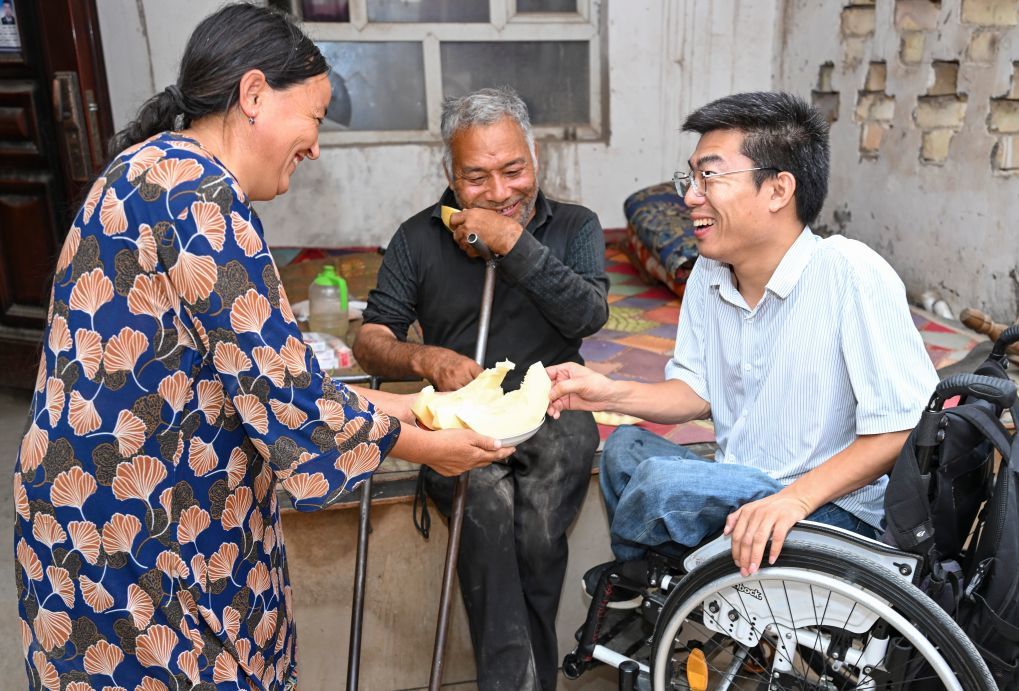 2026年7月26日，李创业（右）到距离诊所不太远的英阿瓦特村上门为残疾村民送药看病，村民端上甜瓜表达谢意。