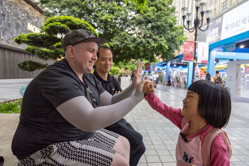 ↑ 4月22日，在重庆市渝中区解放碑商圈，一名中国小女孩和来自爱尔兰的游客互动。