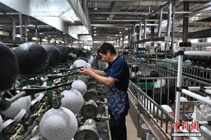 6月18日，安徽省定远县球类产业园一企业生产车间内，工人们加紧赶制足球。图为工人正在对足球进行缠线。　中新社记者 韩苏原 摄