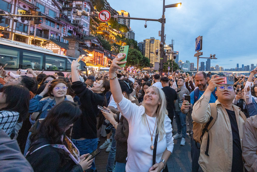 ↑ 4月22日，外籍游客在重庆市渝中区拍摄洪崖洞景区亮灯后的景观。