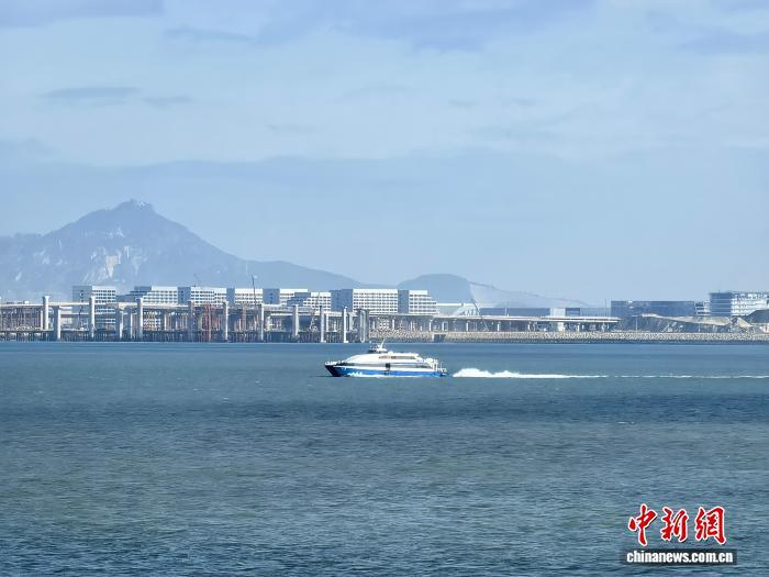 2025年12月27日,一艘经“小三通”航线的渡轮从厦门驶往大金门岛,渡轮后方为正在建设的厦金大桥和厦门翔安国际机场。 中新社记者 刘大炜 摄