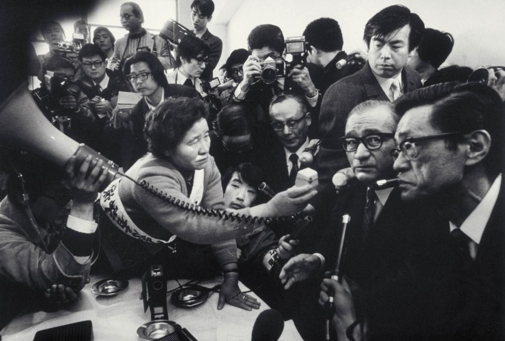 1973年,先天性水俣病患者坂本忍的母亲坂本藤江手持麦克风,向窒素公司总裁岛田贤一要求就年度赔偿金问题作出答复。