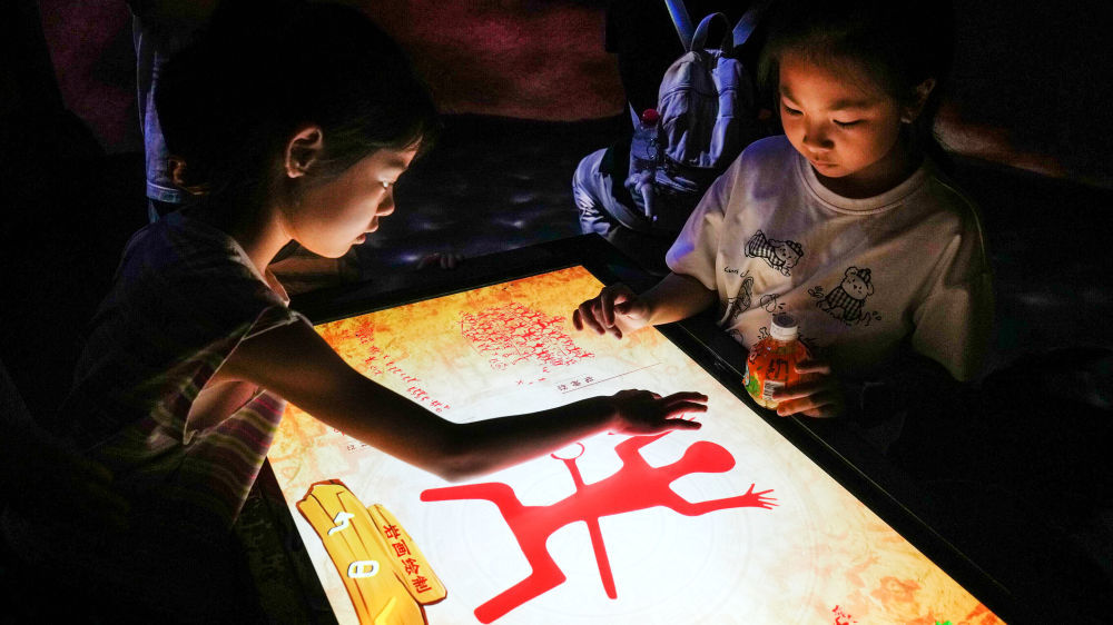 10月2日,在广西壮族自治区博物馆,两名儿童借助智能设备学习制作花山岩画中的图腾。新华社记者 张爱林 摄
