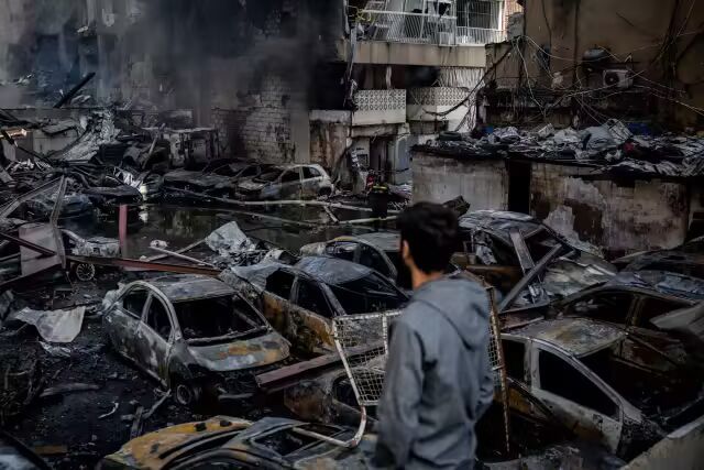 一名男子在以色列空袭贝鲁特后，看着被毁的汽车，建筑物燃烧。