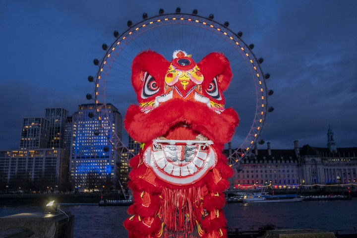 2月16日晚,在英国首都伦敦,演员在亮起红色灯光的“伦敦眼”前表演舞狮。新华社发(史蒂芬·程摄)