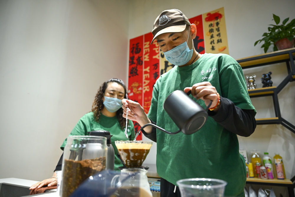 2025年，首家“憨胖儿咖啡”在内蒙古呼和浩特市新城区哲里木路社区开业，为患孤独症和智力残疾的青年提供就业机会，帮助他们融入社会。目前这家公益咖啡馆已在呼和浩特市开设7家门店。这是2026年5月8日，咖啡师小宇（右）在呼和浩特市玉泉区一家憨胖儿咖啡店制作咖啡，他的母亲赵巧花（左）也是店里的一名员工。