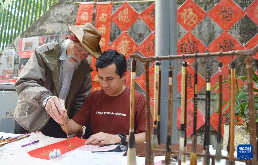 2月13日,在香港楼梯街,郭腾龙(左)教外国朋友用毛笔书写中文名字。新华社记者 陈铎 摄