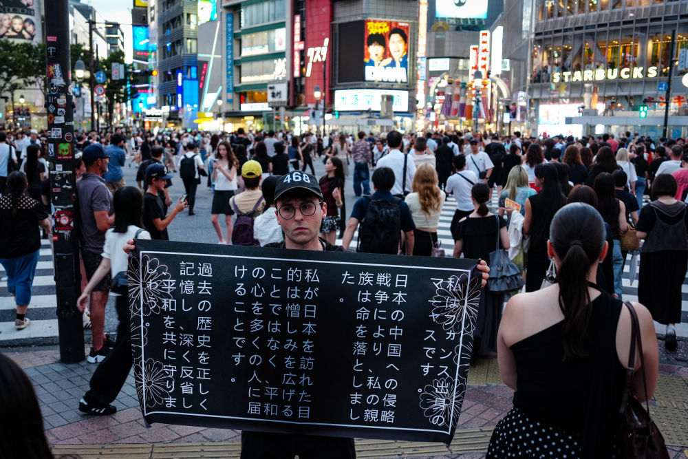 8月5日，在日本东京涩谷街头，法国青年马库斯&middot;德雷特斯手举横幅，呼吁日本社会正视对外侵略历史。新华社记者贾浩成摄