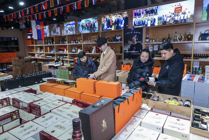 1月30日，在浙江义乌中国进口商品城一家店铺内，店员给顾客推荐塞尔维亚葡萄酒。新华社记者 徐昱 摄