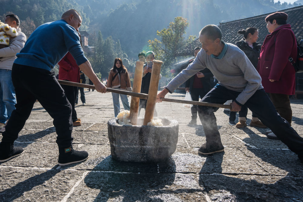 ↑1月10日,在湖北省宣恩县沙道沟镇两河口村彭家寨,村民为游客打糍粑。新华社发(文林摄)