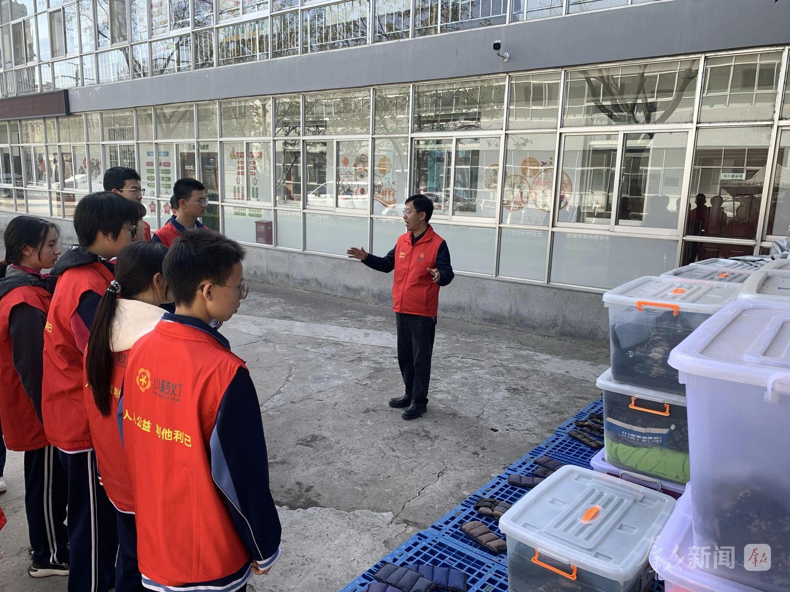 4月1日,在咸阳市小桔灯公益服务中心,郭恩伟(右一)向同学们介绍募捐衣物箱的整理方法及用途。