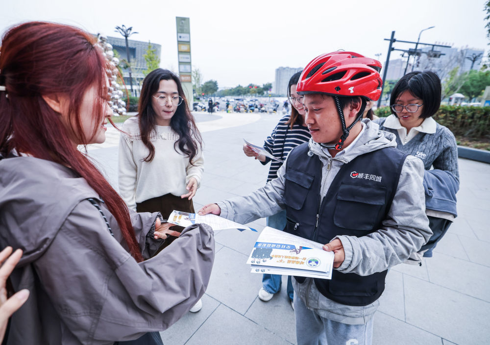 2025年11月7日，在浙江省诸暨市陶朱街道商业综合体的暖心关爱服务点，“小哥志愿服务队”的志愿者给市民发放防范电信网络诈骗、消防安全知识等宣传单。新华社记者 徐昱 摄