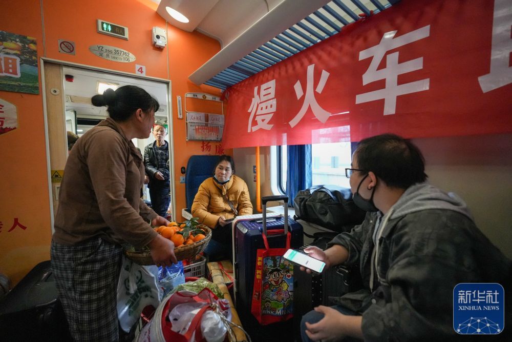 ↑ 2月12日,在7272次列车车厢内,来自湖南的村民(左)和乘客进行交易。新华社发(龙建睿 摄)