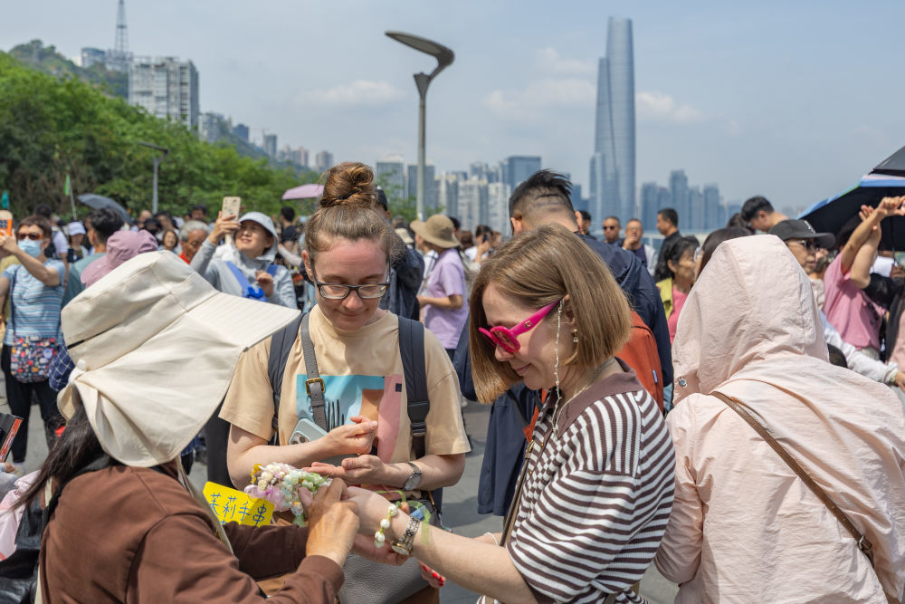 ↑ 4月23日，在重庆市渝中区李子坝观景平台，外籍游客购买茉莉花手串。